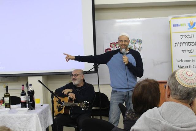 גיל קופטש מרצה עם מיקרופון מול מסך הקרנה